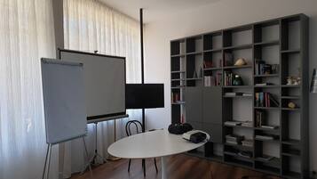 Una sala de conferencias con una mesa blanca, un proyector, una pizarra y una estantería llena de libros y adornos.
