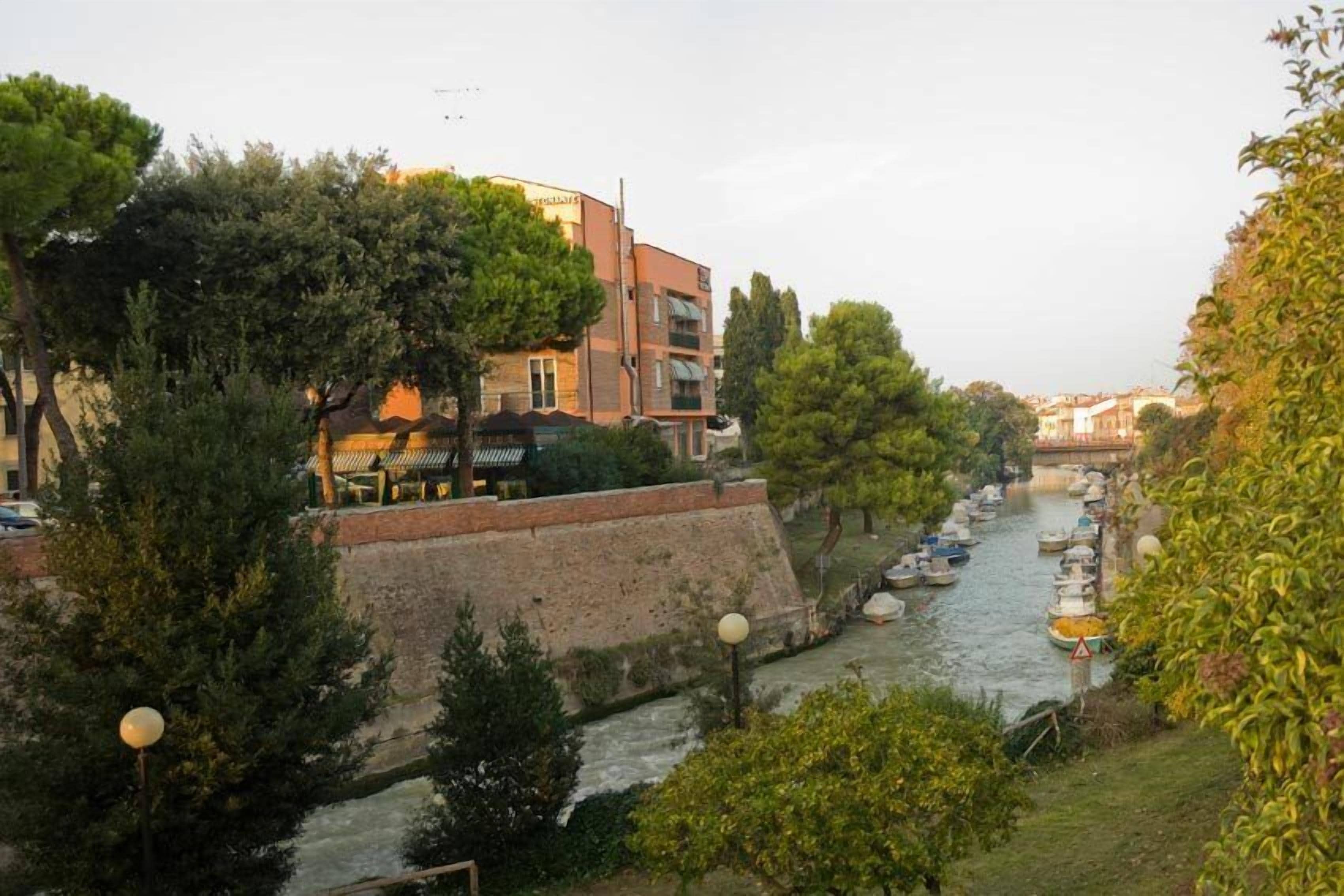 A canal with boats, a brick wall, and buildings with balconies.