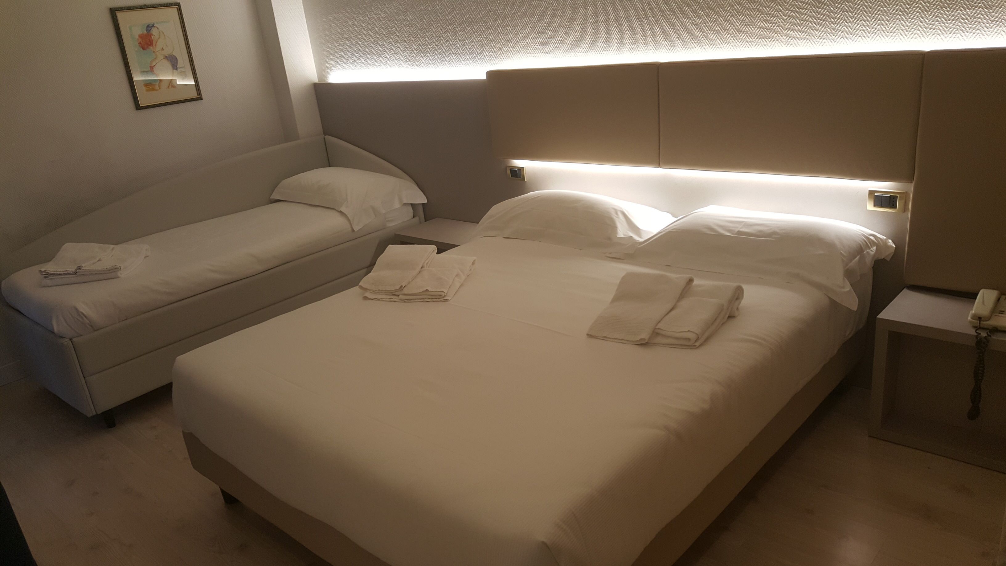 Quarto de hotel com duas camas, uma mesa de cabeceira com telefone e luminária na parede.