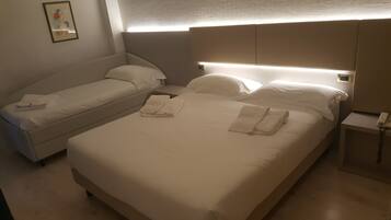 Quarto de hotel com duas camas, uma mesa de cabeceira com telefone e luminária na parede.