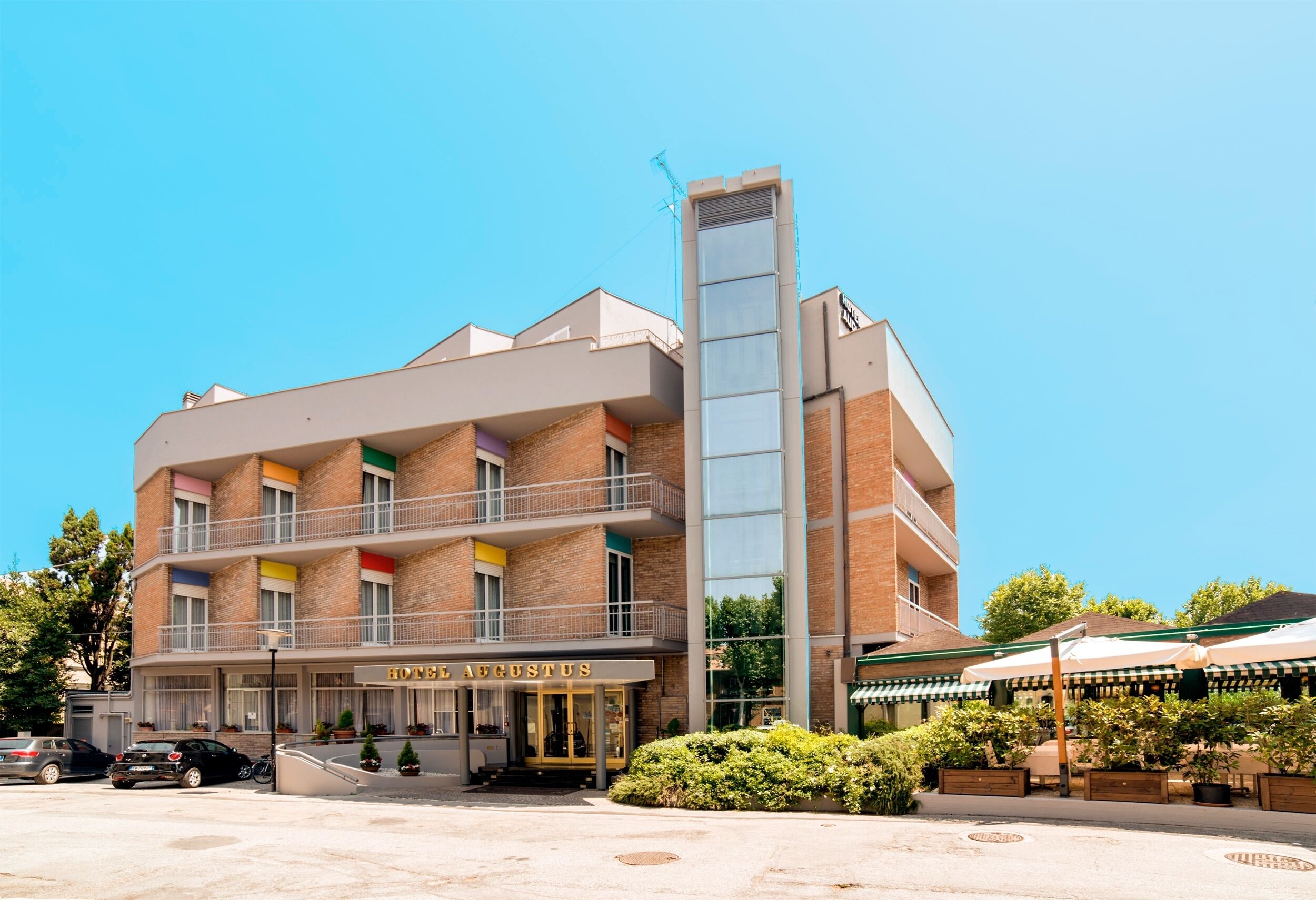 Ein Hotel mit moderner Architektur, das durch einen markanten, hohen Glasbau und einen Eingangsbereich mit der Beschriftung "HOTEL AUGUSTUS" gekennzeichnet ist.