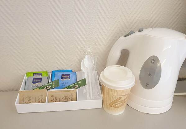 Una tetera eléctrica blanca, un vaso de café desechable y una bandeja con diversos productos envasados.