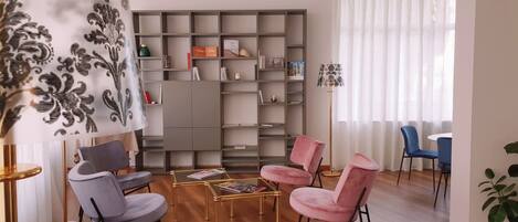 A living room with a grey sofa, a pink chair, a coffee table, a bookshelf, and a floor lamp.