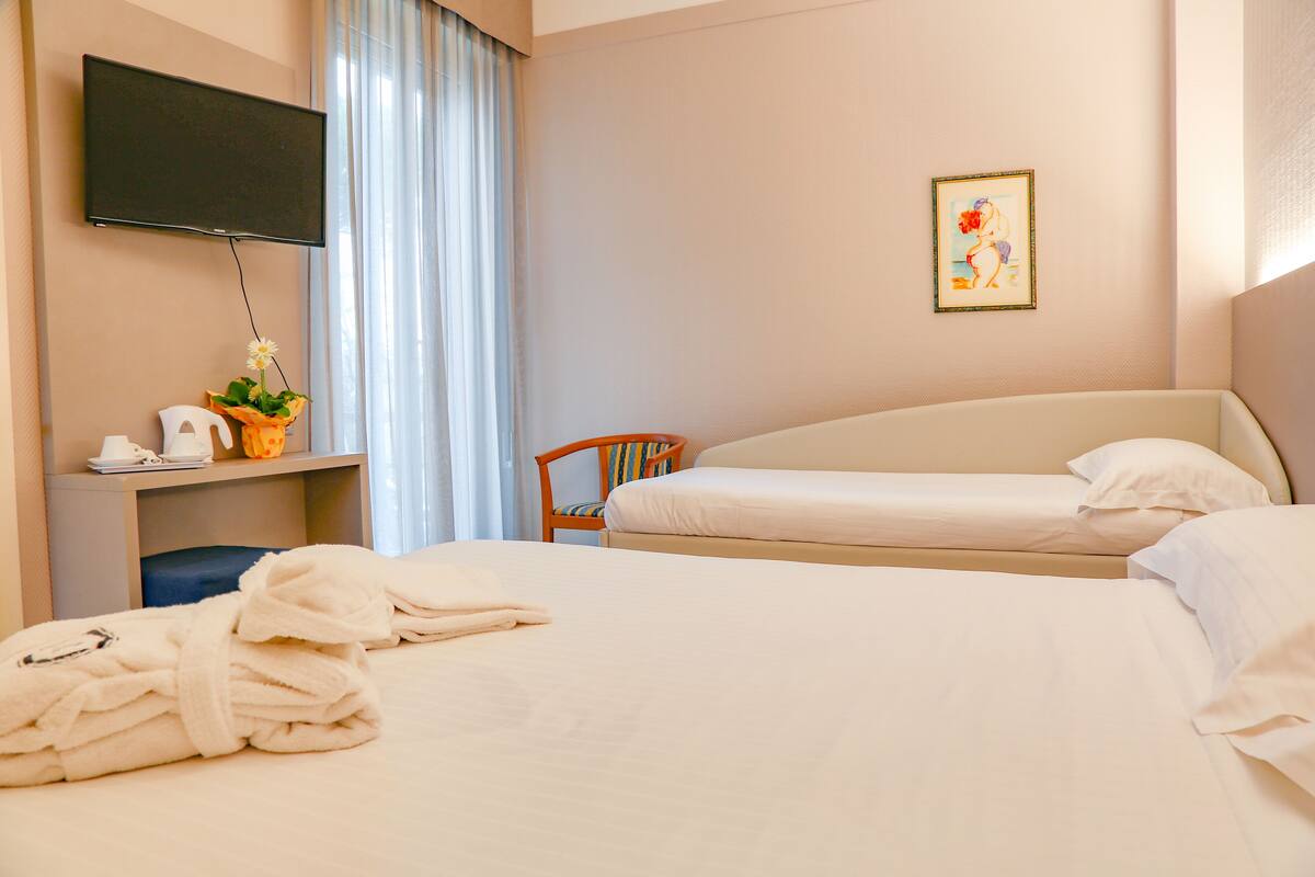A hotel room with two beds, a desk with a TV, a chair, and a painting on the wall.