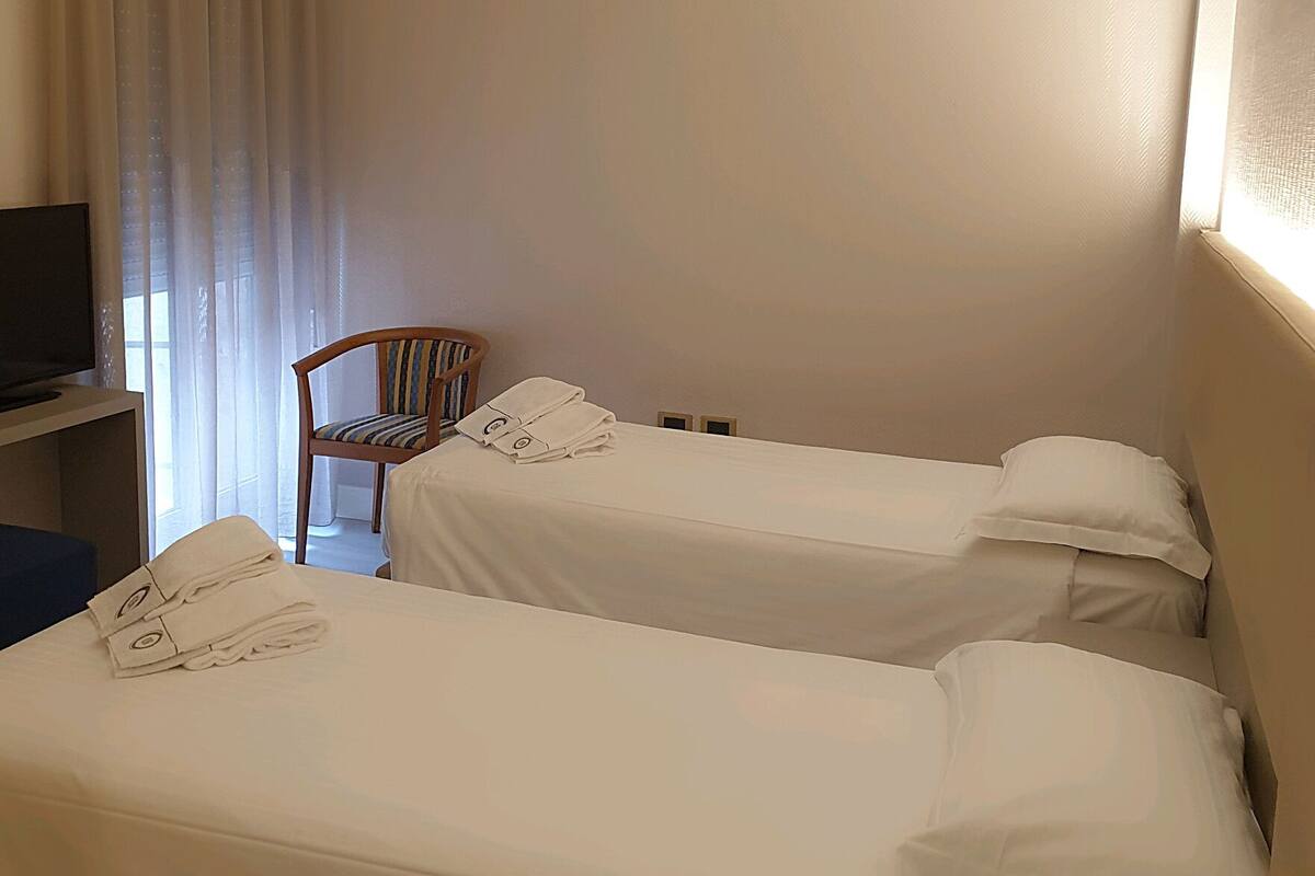 A hotel room with two single beds, a chair, a desk, and a television.
