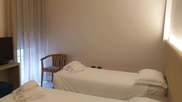 A hotel room with two single beds, a chair, a desk, and a television.