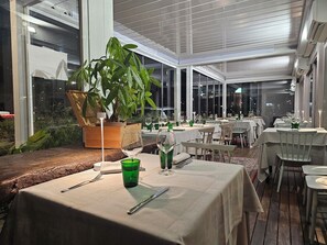 Un restaurante con mesas dispuestas para comer, una planta grande en maceta y vistas a través del techo de cristal.