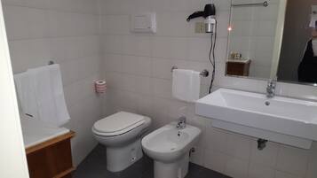 Ein kleines, sauberes Badezimmer mit Toilette, Bidet und Waschbecken. Eine Handtuchstange, ein Papiertuchspender und ein Fön sind an der Wand angebracht.