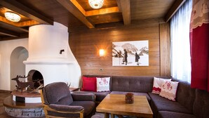 Un interior acogedor con chimenea de piedra, vigas de madera y un gran ventanal con cortinas rojas.