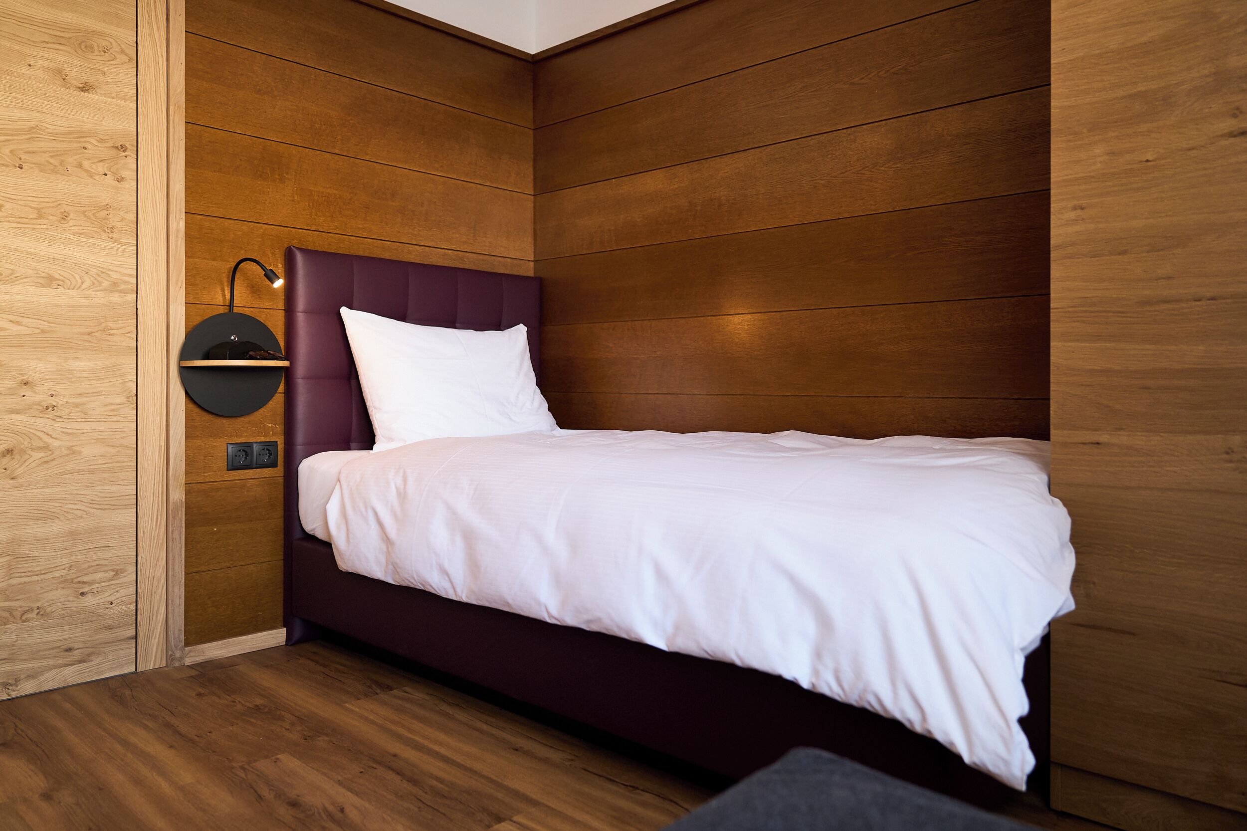 A modern bedroom with a wooden wall panel design, a purple headboard, and a white bedspread.