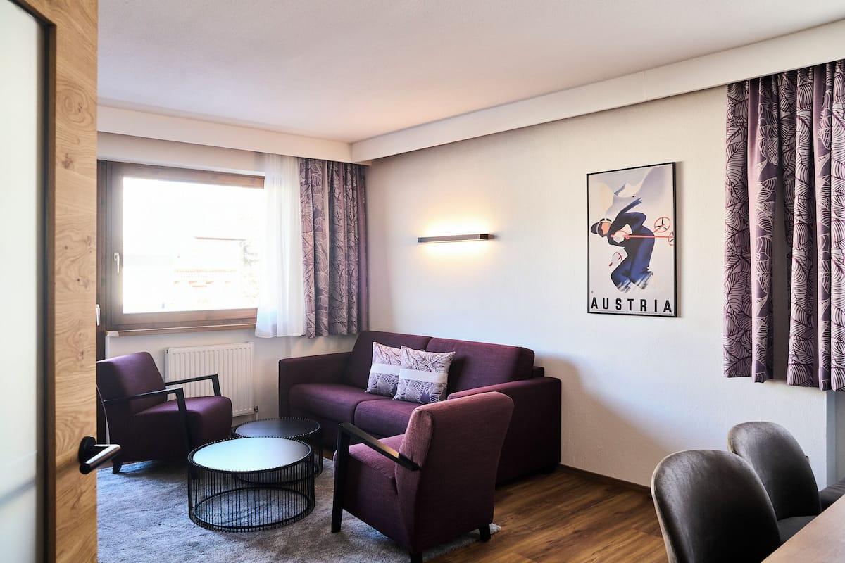 Ein modernes Wohnzimmer mit einer Couch, Sesseln, einem Couchtisch und einer Wandleuchte.