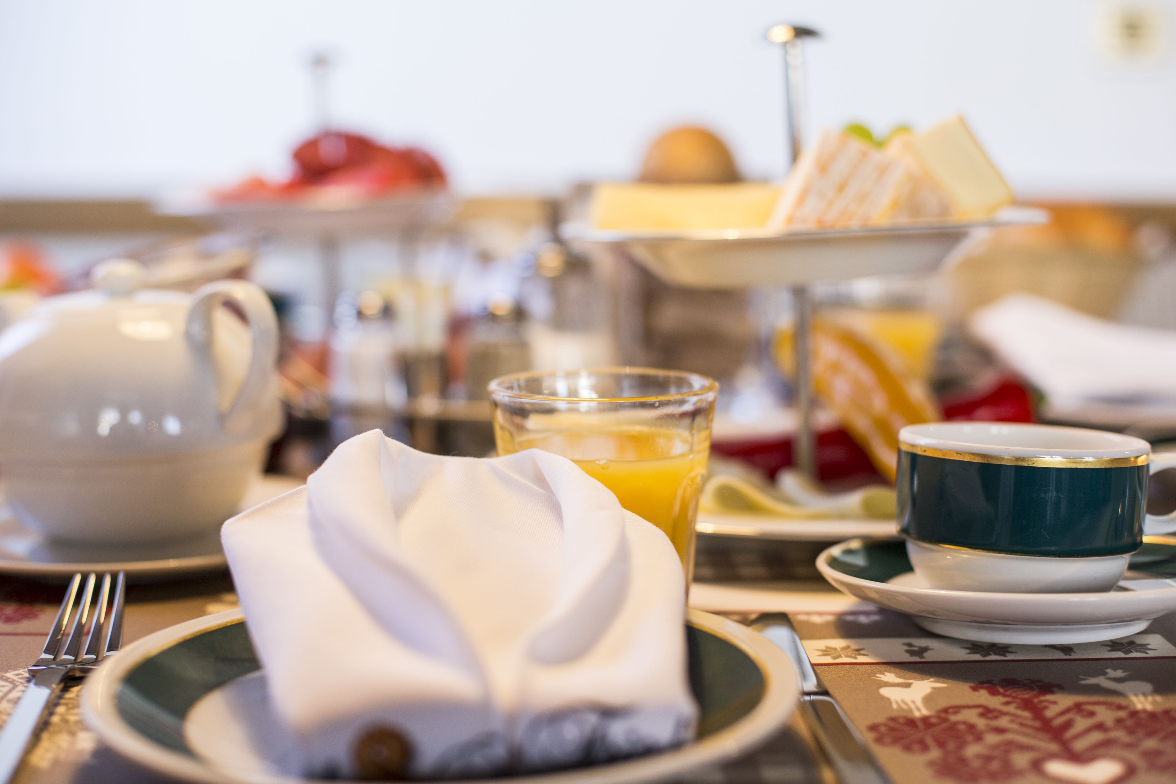 Et morgenbord med te, appelsinjuice, en kop og en tallerken med serviet.