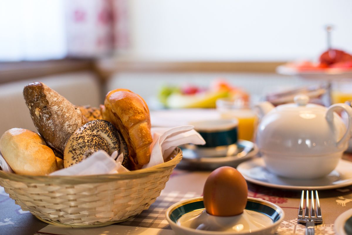A breakfast setting with a basket of bread, a teapot, and a plate with an egg.