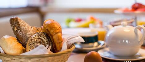 A breakfast setting with a basket of bread, a teapot, and a plate with an egg.