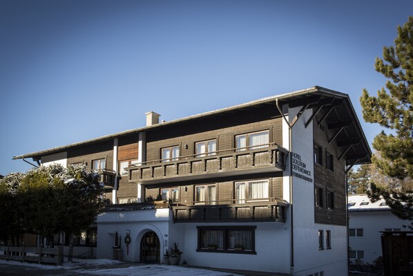 Un hotel de dos pisos con un balcón en el nivel superior, cielo despejado y suelo cubierto de nieve.