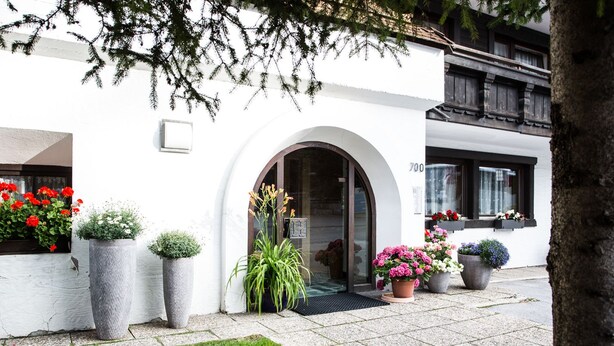 Un edificio blanco con un gran arco de entrada, plantas en macetas y jardineras en los alféizares de las ventanas.