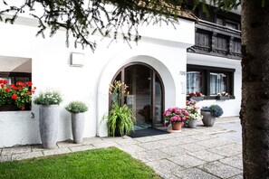 Un edificio blanco con un gran arco de entrada, plantas en macetas y jardineras en los alféizares de las ventanas.