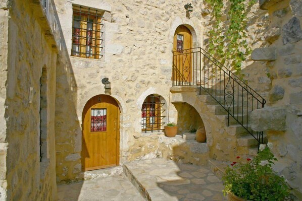 A stone building with wooden doors and windows, a staircase with metal railings, and potted plants.