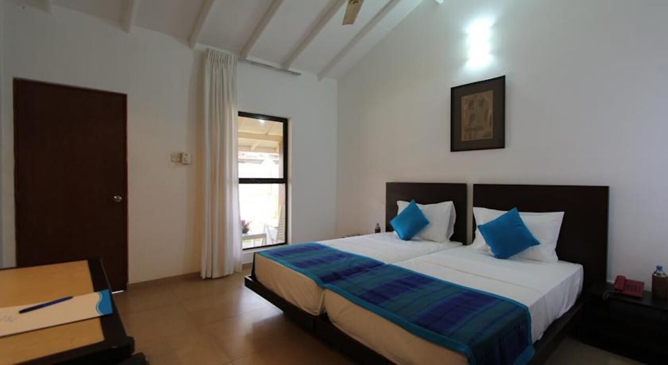 A hotel room with two beds, a desk, a window with curtains, and a framed picture on the wall.