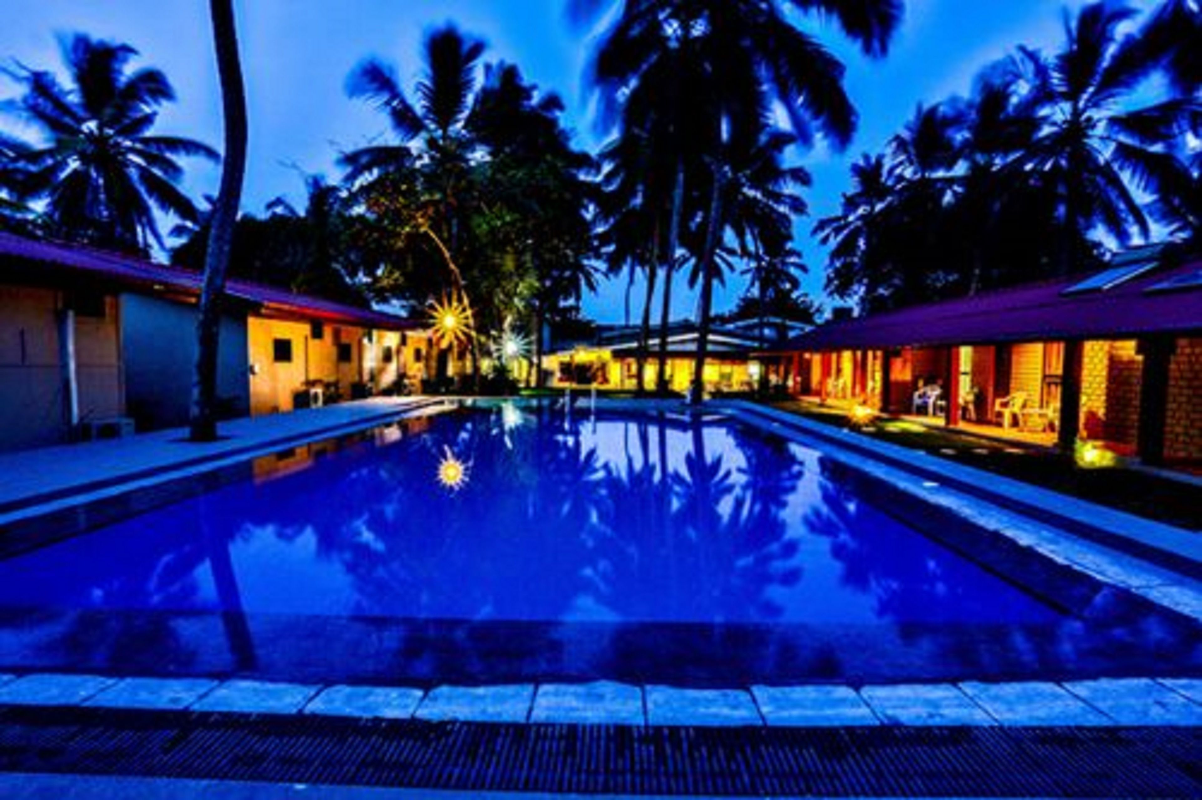 Piscina com palmeiras e edifícios ao fundo.