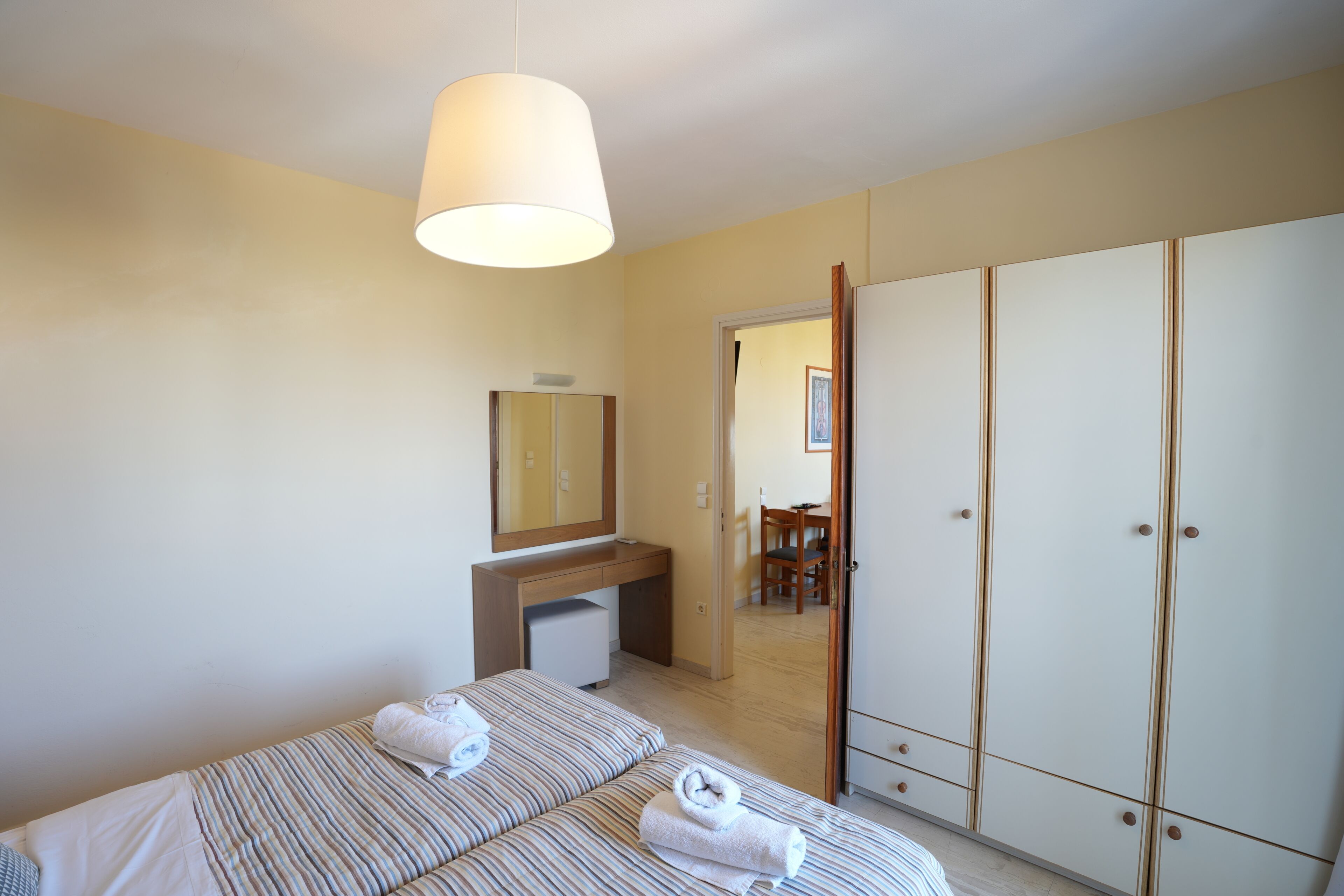 A bedroom with two beds, a desk, a mirror, and a wardrobe.