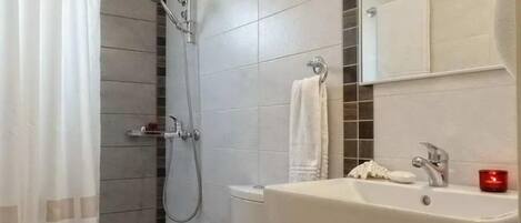 A bathroom with a shower, toilet, sink, and a mirror.