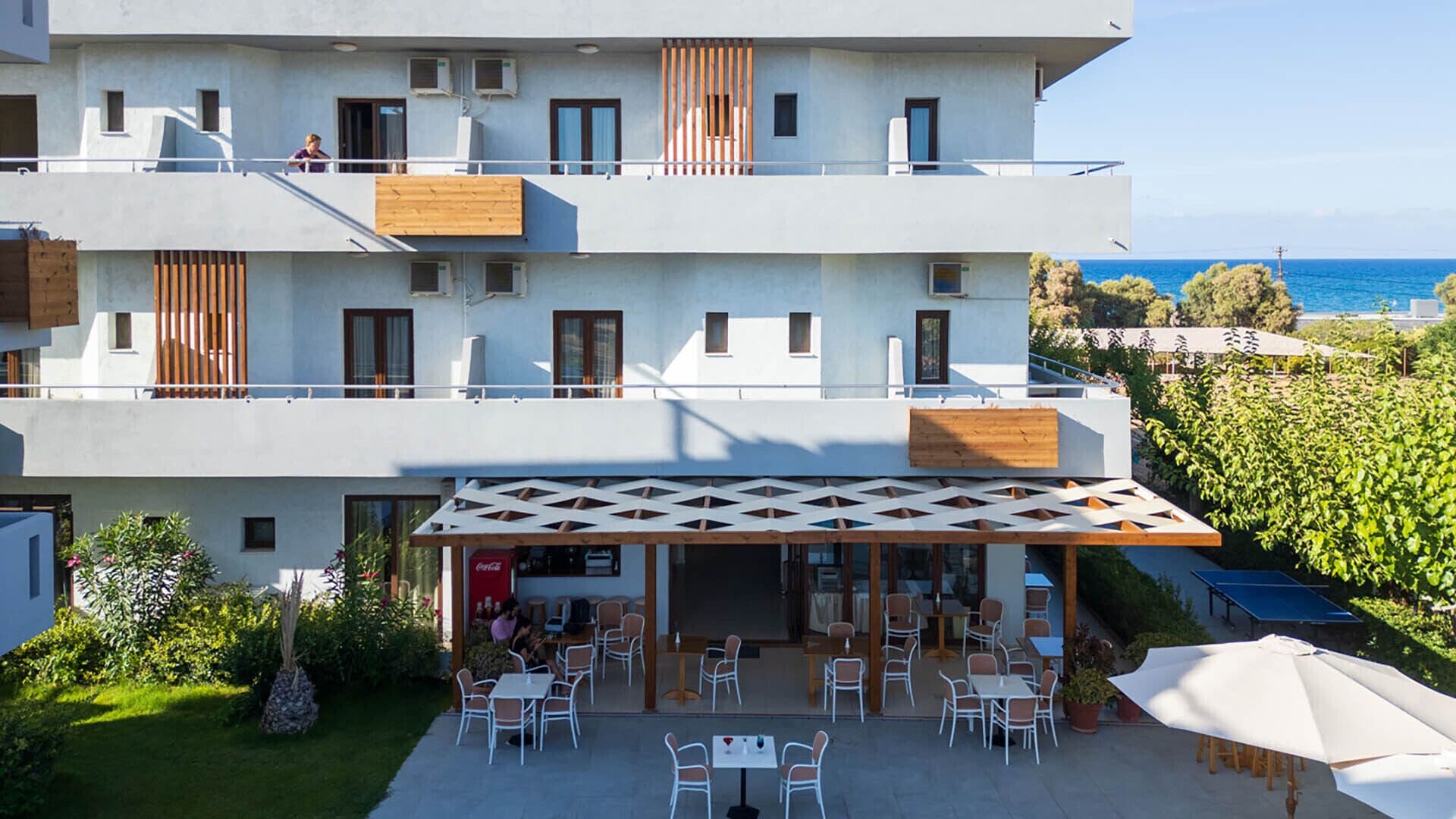 A multi-story hotel with outdoor seating and a view of the sea.