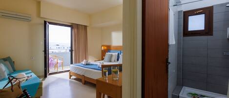 A hotel room with a balcony, a bed, a desk with a chair, and a bathroom with a shower and toilet.