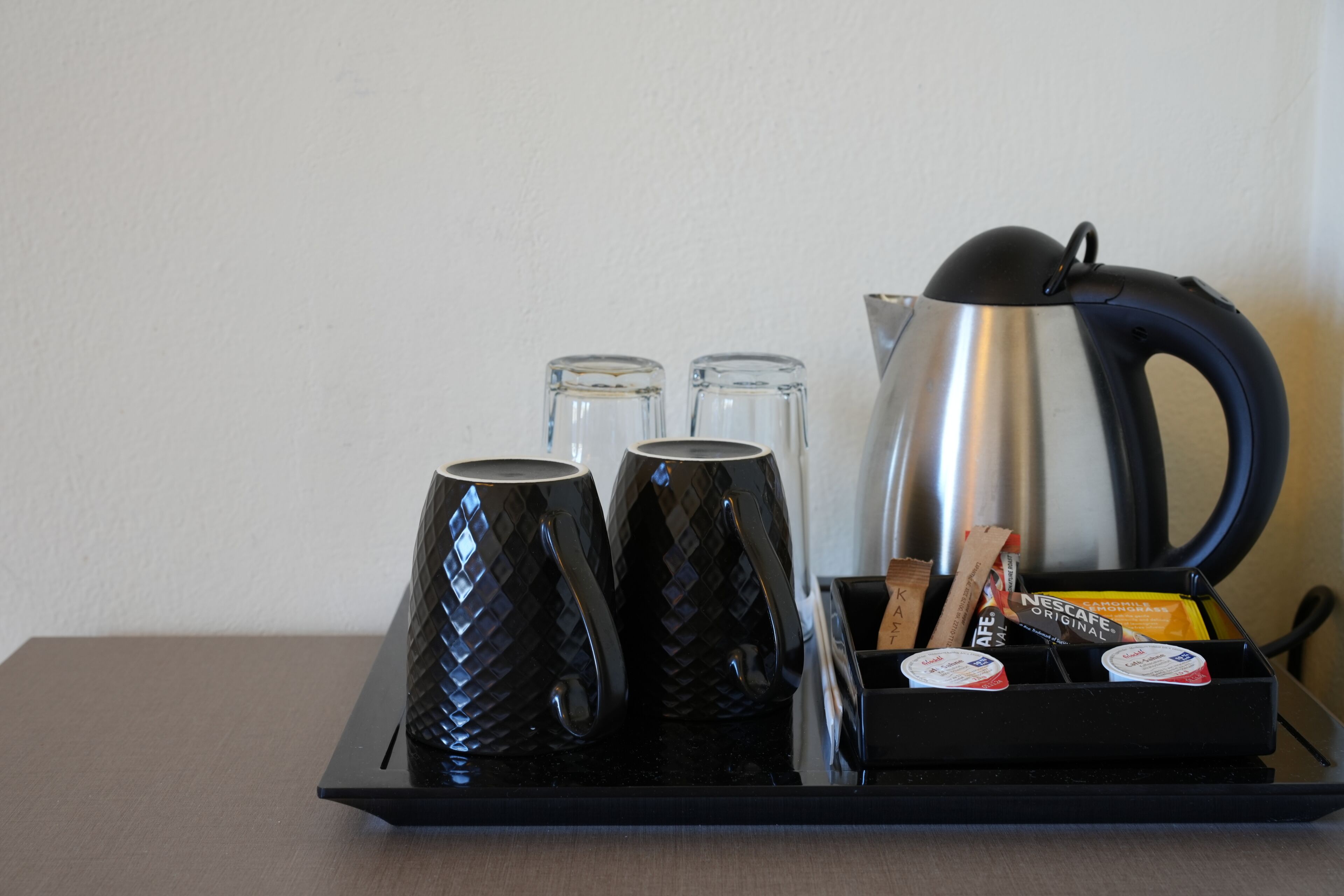Ein Tablett mit einer Kaffeemaschine, drei Tassen, zwei Gläsern und einer Packung Nescafe Original Kaffee.