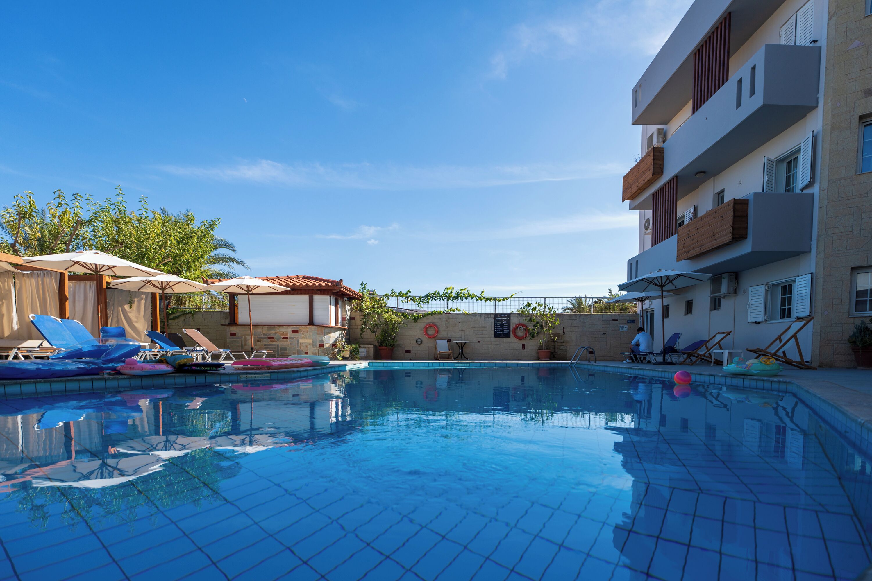 A swimming pool with lounge chairs and umbrellas, surrounded by buildings with balconies and windows.