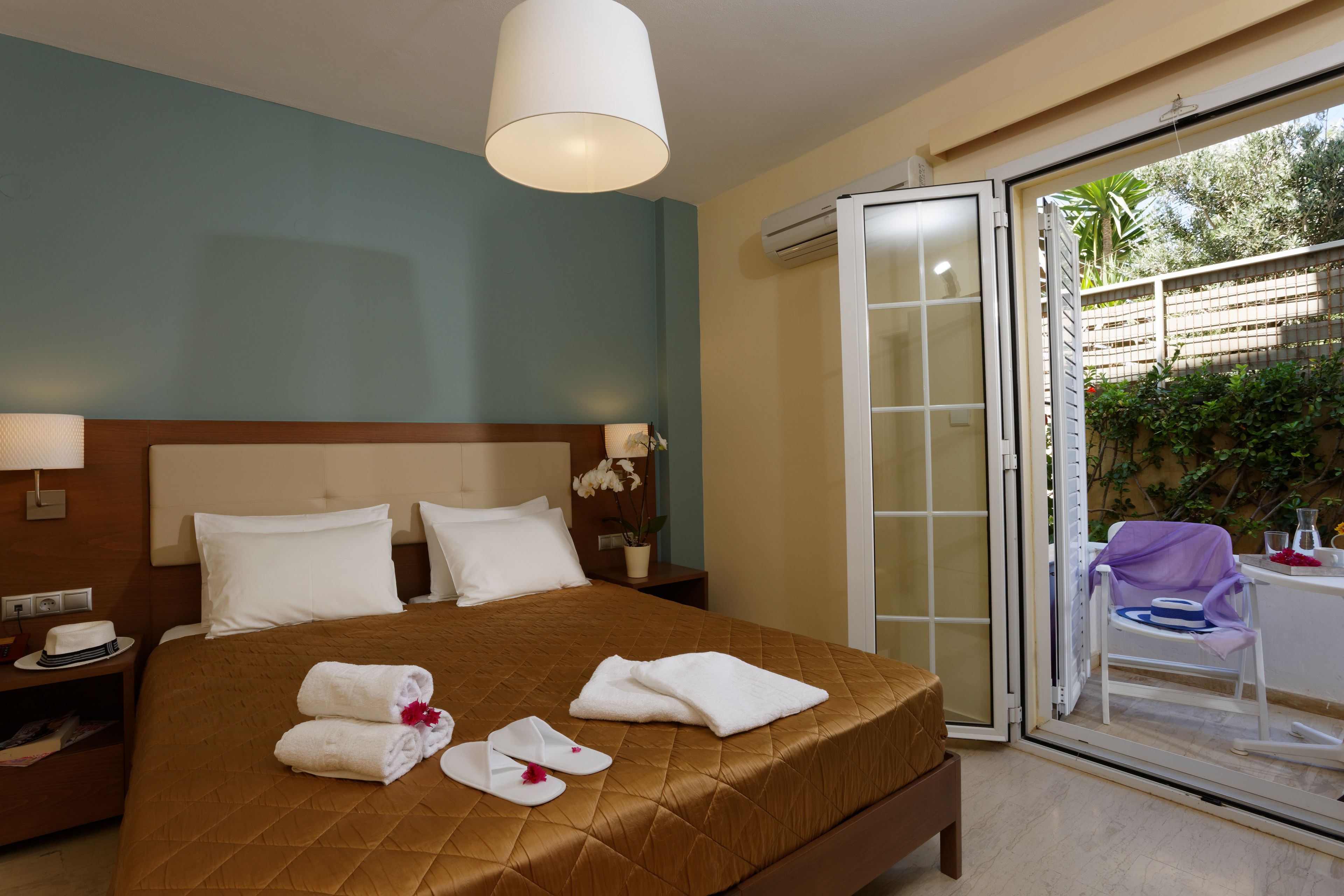 Habitación de hotel con una cama, una mesita de noche, una mesa con una silla y un cristalera corredera que da a un área exterior.