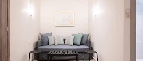 A small, modern living room with a grey sofa, two black side tables, and a framed picture on the wall.