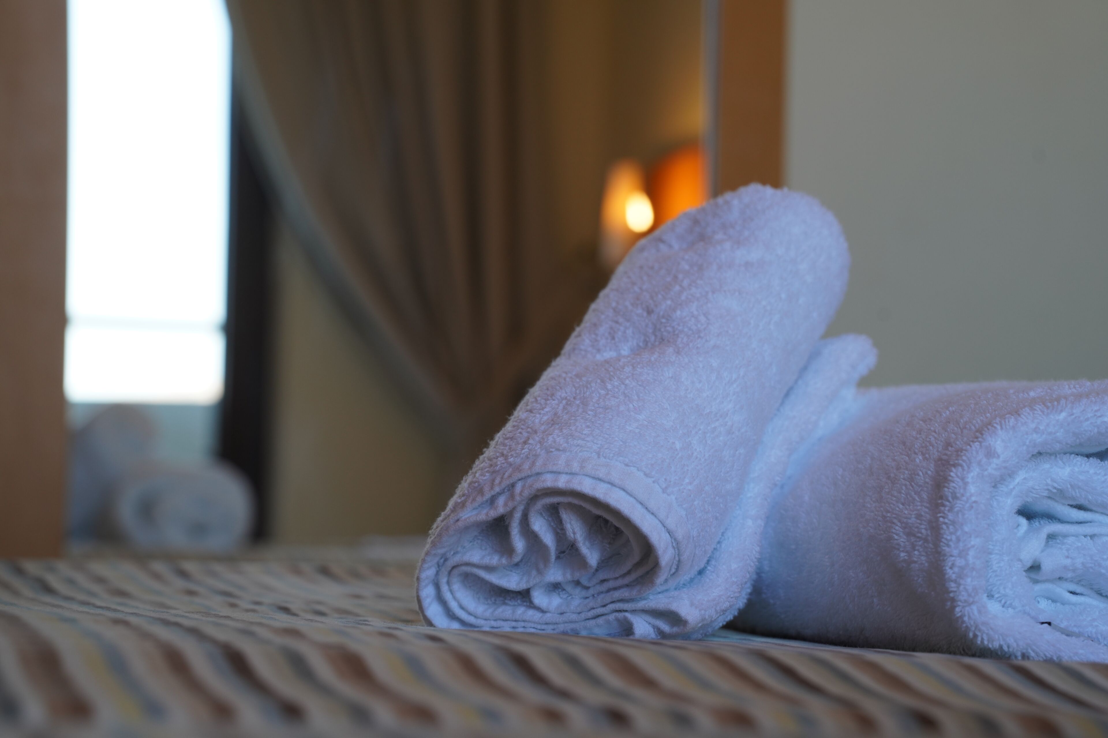 Une serviette soigneusement pliée est posée sur un lit recouvert d’une couvre-lit à motifs.