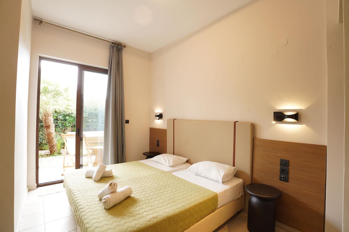Une chambre d’hôtel avec un lit, une table de chevet, une lampe, une porte-fenêtre coulissante donnant sur le balcon et une vue sur la verdure environnante.