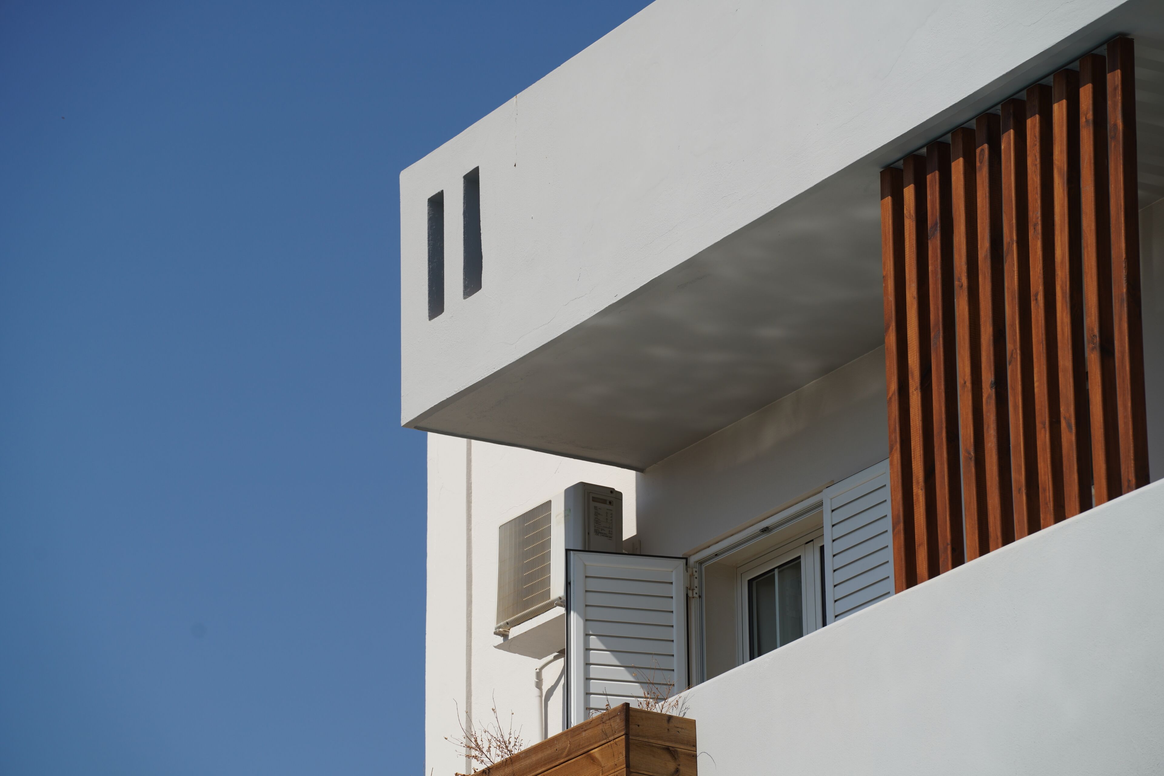 A modern building with a white facade, a wooden slatted window, and an air conditioning unit.