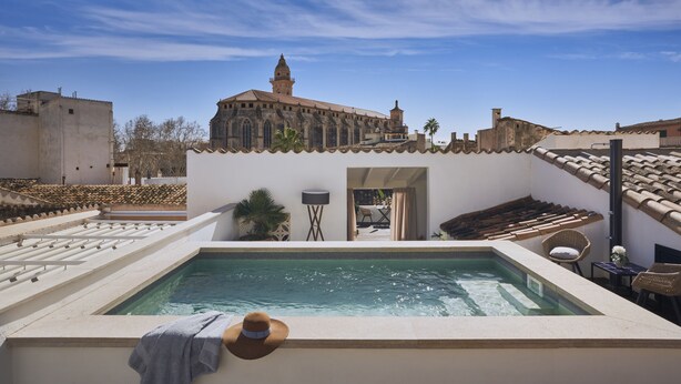 Una piscina en la azotea con vistas a un edificio histórico, mobiliario exterior y cielo despejado.