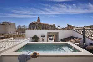 Una piscina en la azotea con vistas a un edificio histórico, mobiliario exterior y cielo despejado.