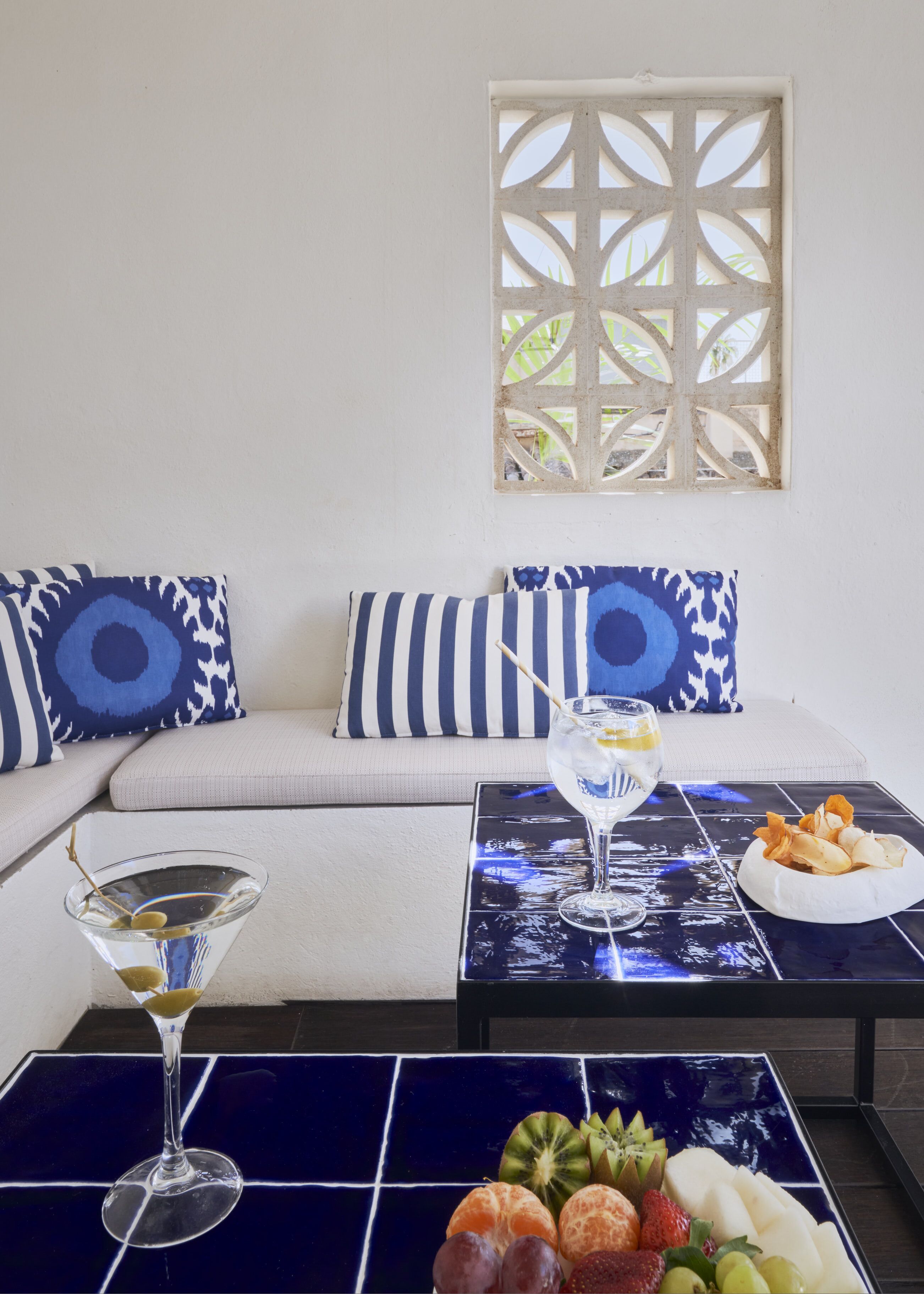 Una sala de estar moderna con un sofá, dos almohadones decorativos, una mesa de centro con una bandeja de frutas y una copa de martini.