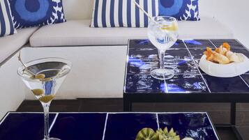 Una sala de estar moderna con un sofá, dos almohadones decorativos, una mesa de centro con una bandeja de frutas y una copa de martini.