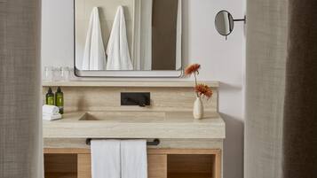 Een moderne badkamer met een houten wastafelmeubel, een grote spiegel en een kleine vaas met bloemen.