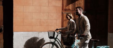 Una persona pasea en bicicleta al pasar por un edificio con pared de ladrillo y puerta de madera.