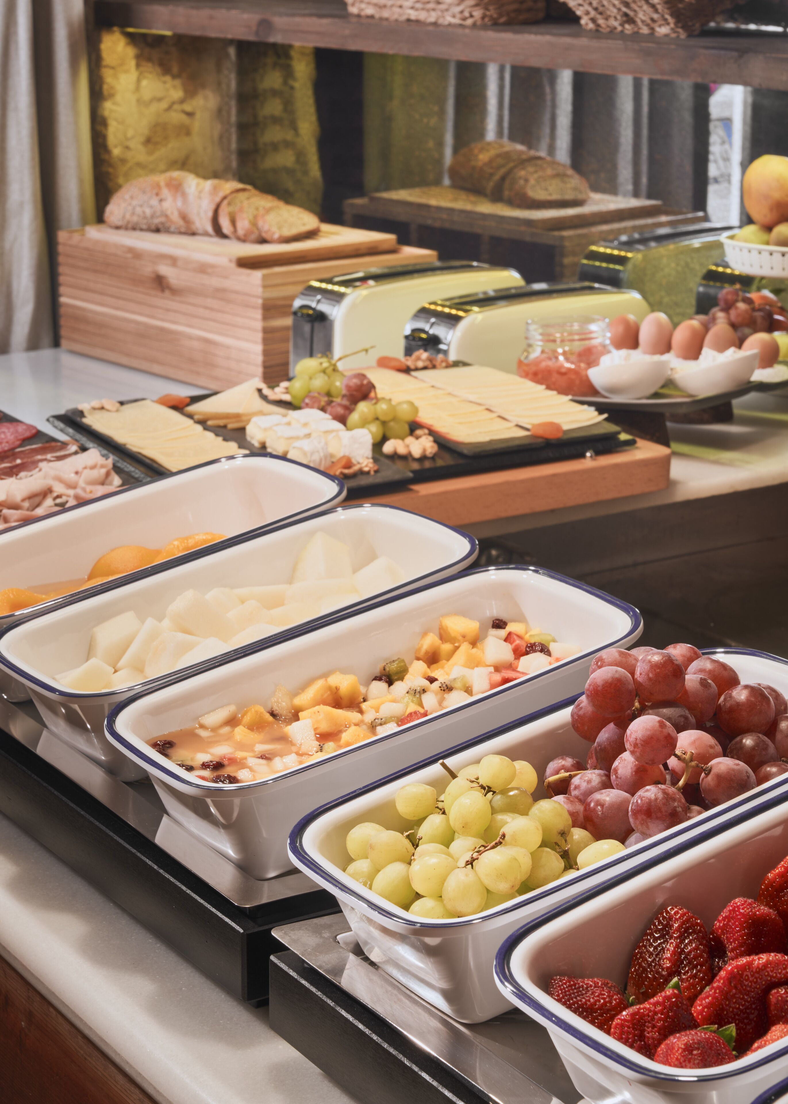 Un bufé con diversos alimentos, entre ellos frutas, quesos y embutidos.