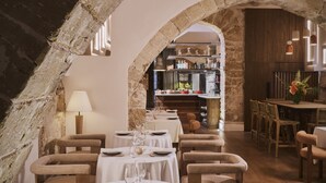 Un restaurante con mesas y sillas redondas, un techo de piedra abovedado y una zona de bar visible a través de un arco.