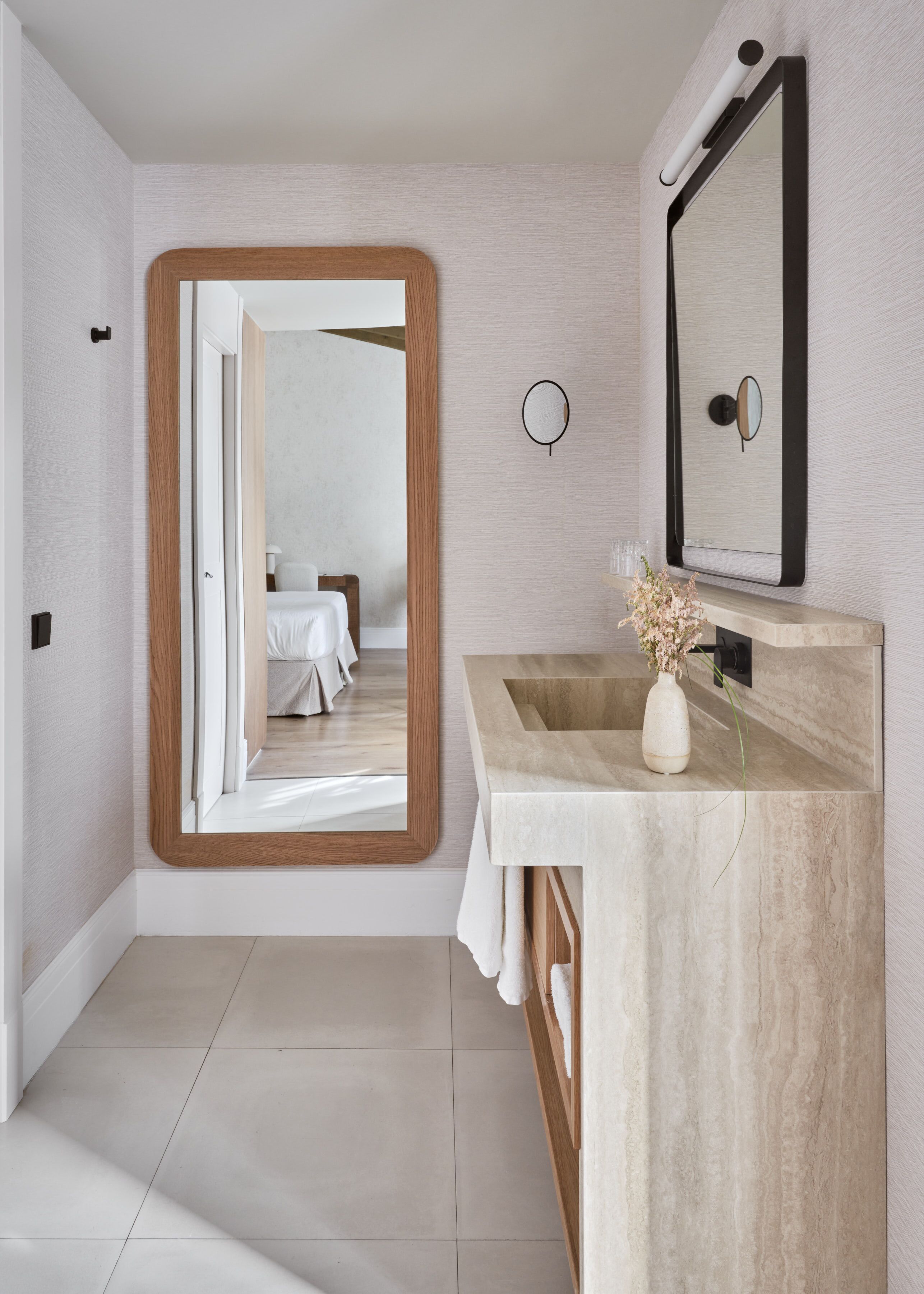 Un baño moderno con un espejo grande, un tocador de madera y vista al dormitorio.