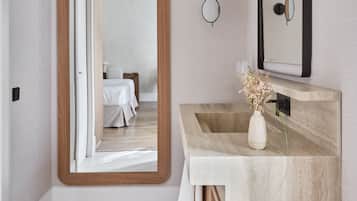 Un baño moderno con un espejo grande, un tocador de madera y vista al dormitorio.
