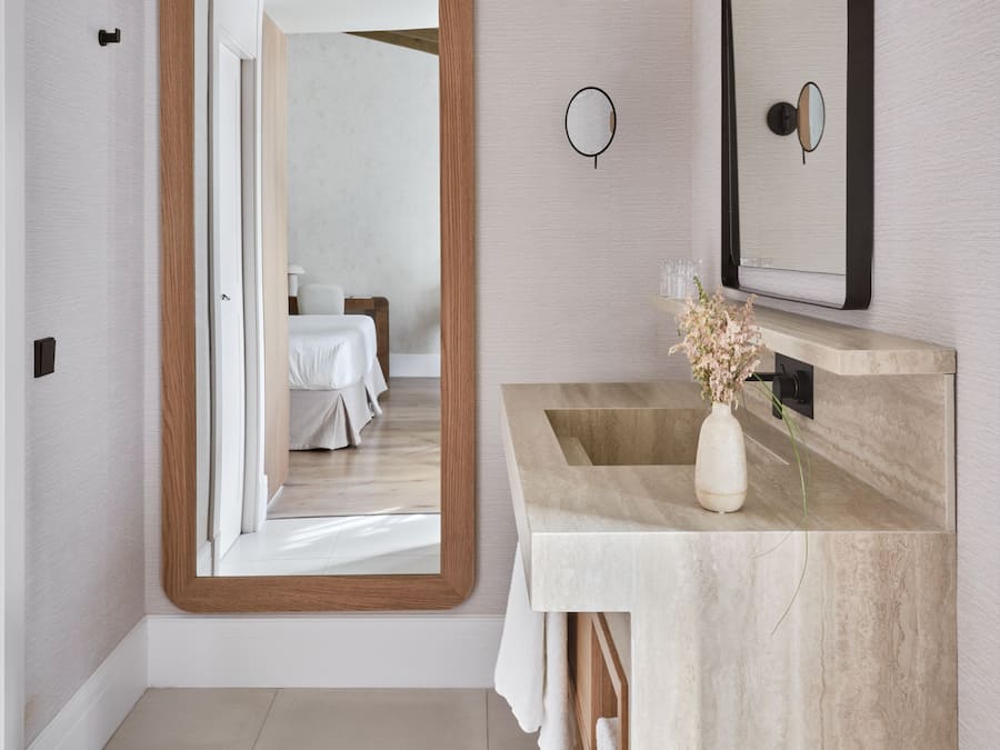 Un baño moderno con un espejo grande, un tocador de madera y vista al dormitorio.