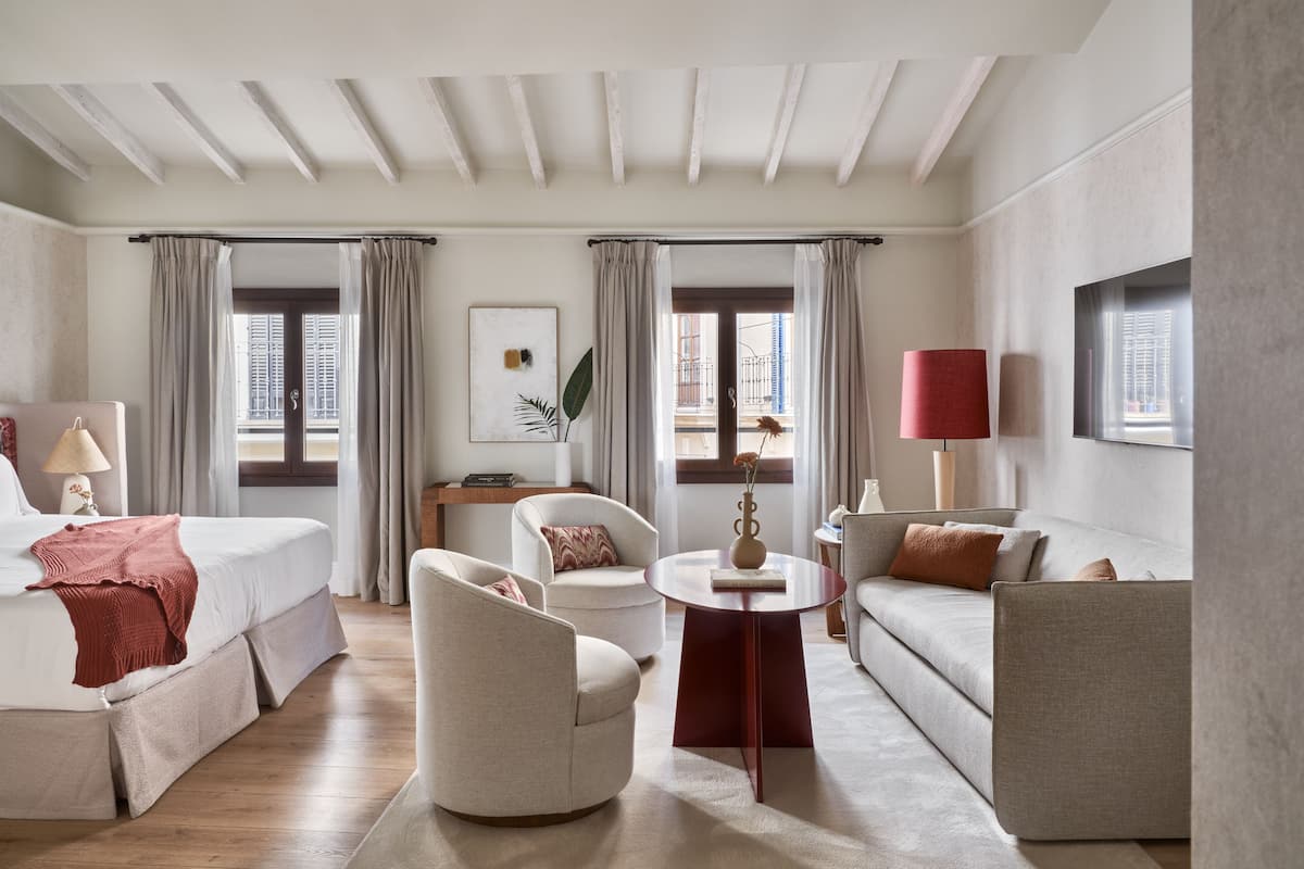 A hotel room with a bed, two armchairs, a sofa, a small table, and a TV.