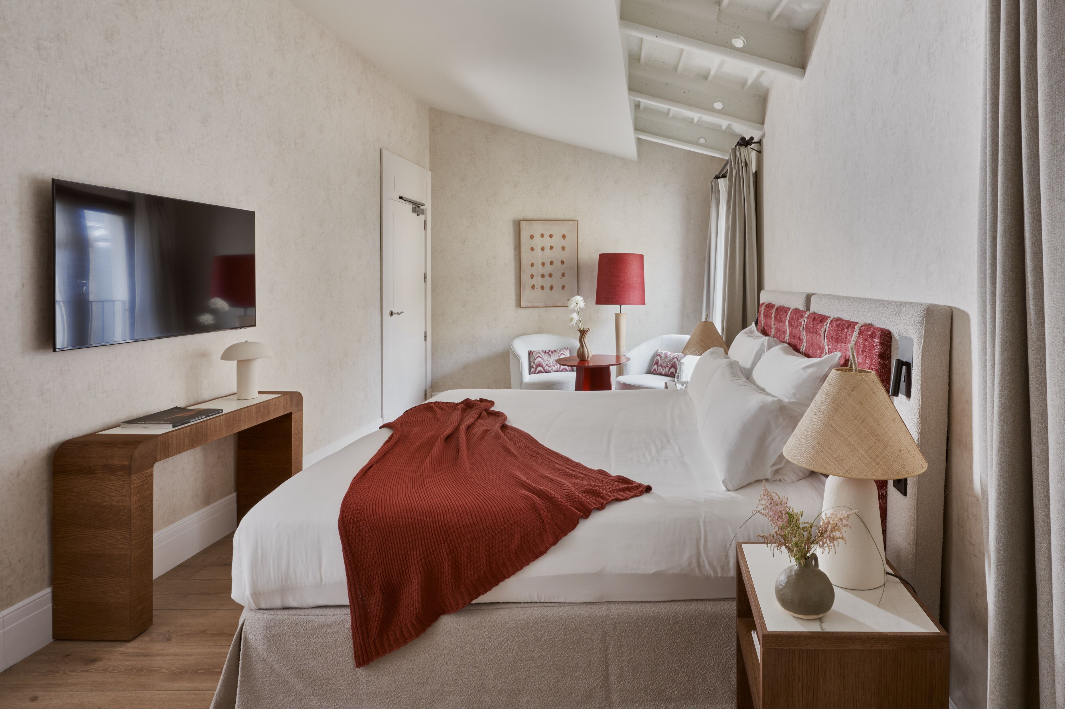 Un dormitorio moderno con cama, mesita de noche, lámpara y un televisor de pantalla plana montado en la pared.
