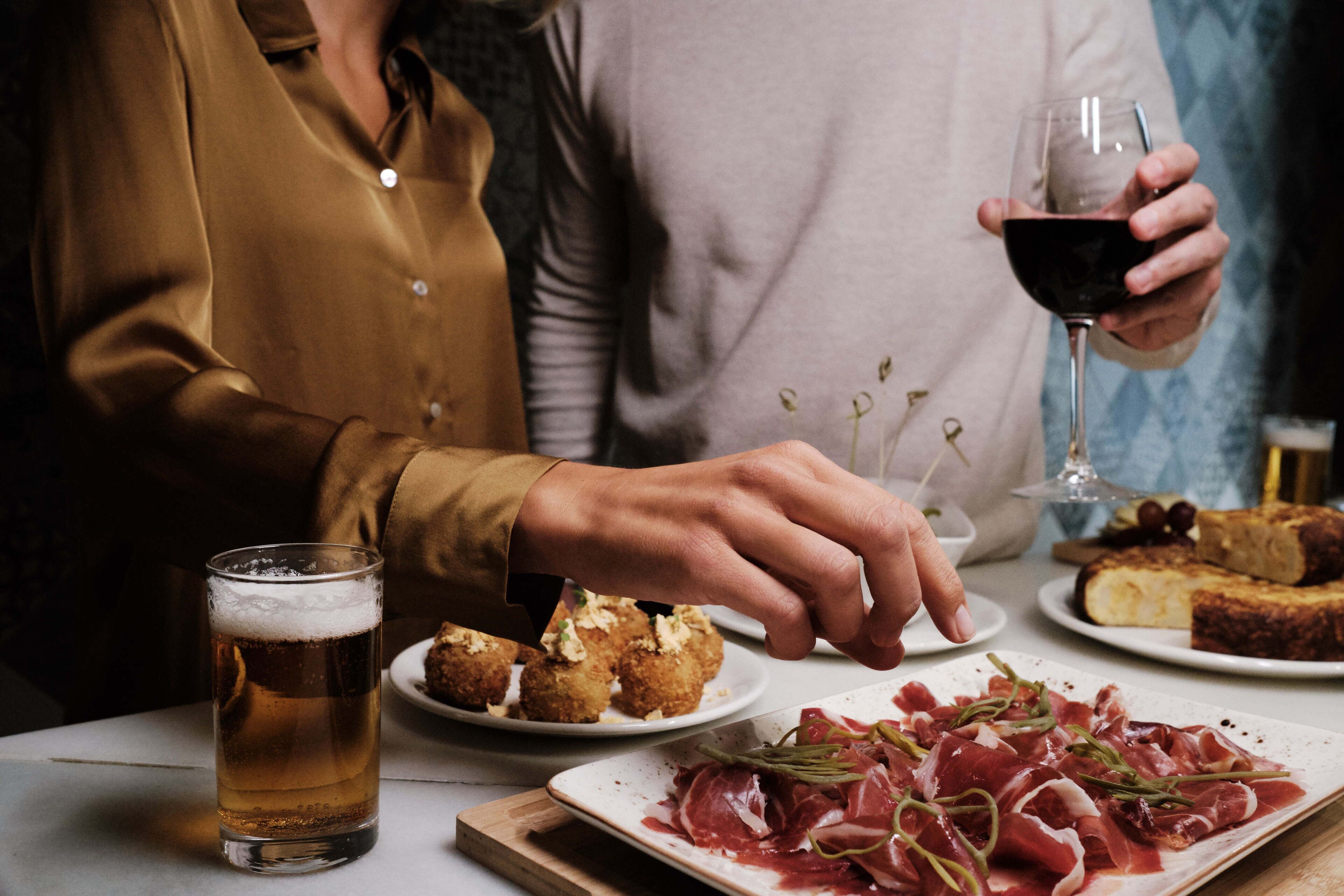 Una mesa de comedor con una cerveza, un plato de comida y una copa de vino tinto.