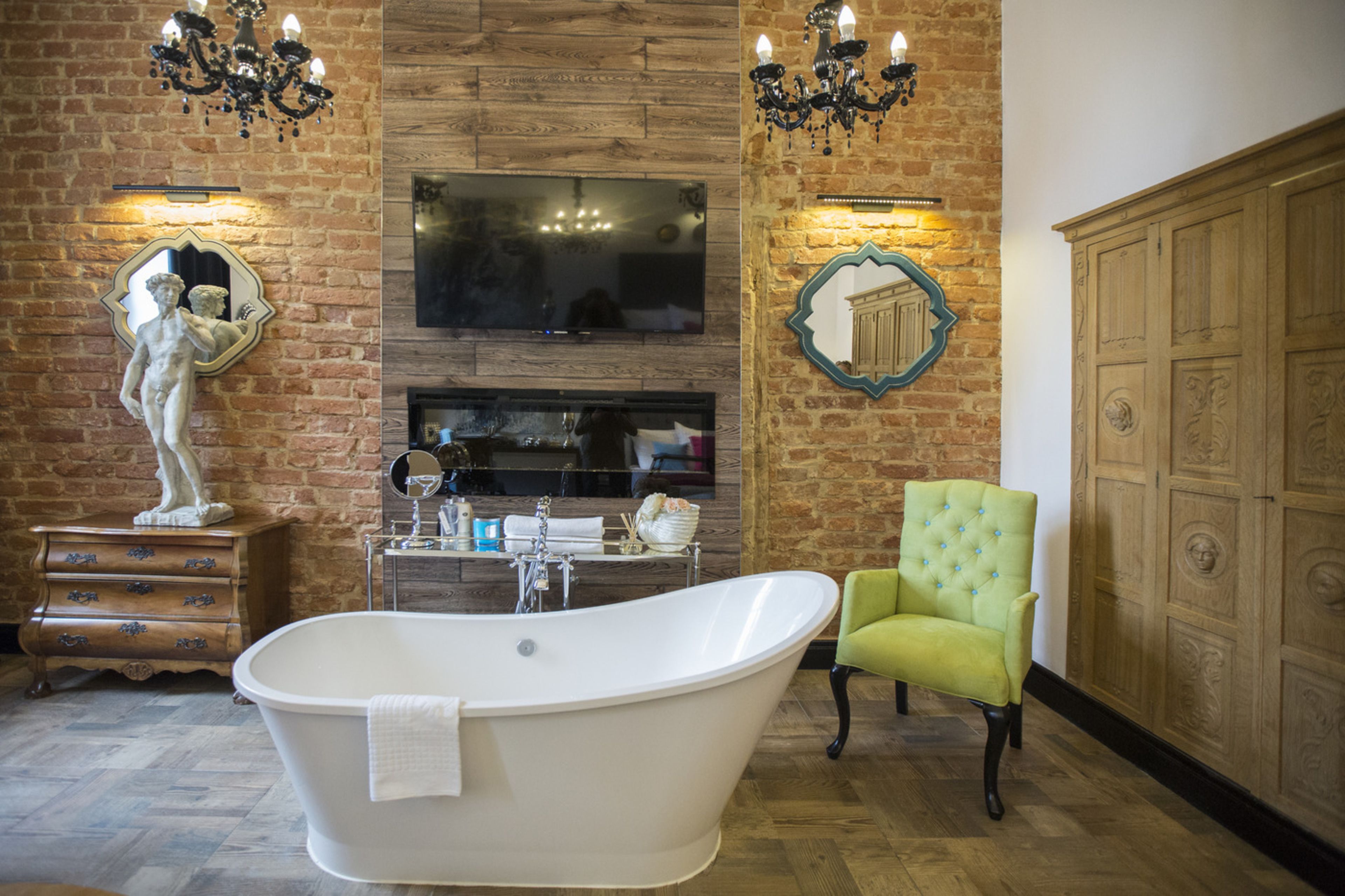 A bathroom with a freestanding bathtub, a green armchair, a wooden cabinet, and a mirror with a decorative frame.